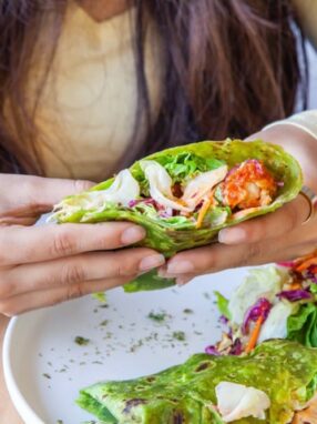 Osoba trzymająca zielony wrap z warzywami i kurczakiem