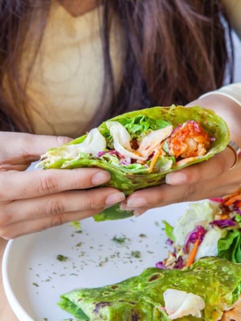 Osoba trzymająca zielony wrap z warzywami i kurczakiem