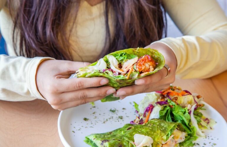 Osoba trzymająca zielony wrap z warzywami i kurczakiem