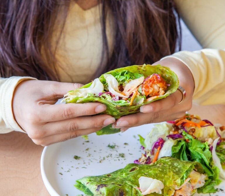 Osoba trzymająca zielony wrap z warzywami i kurczakiem